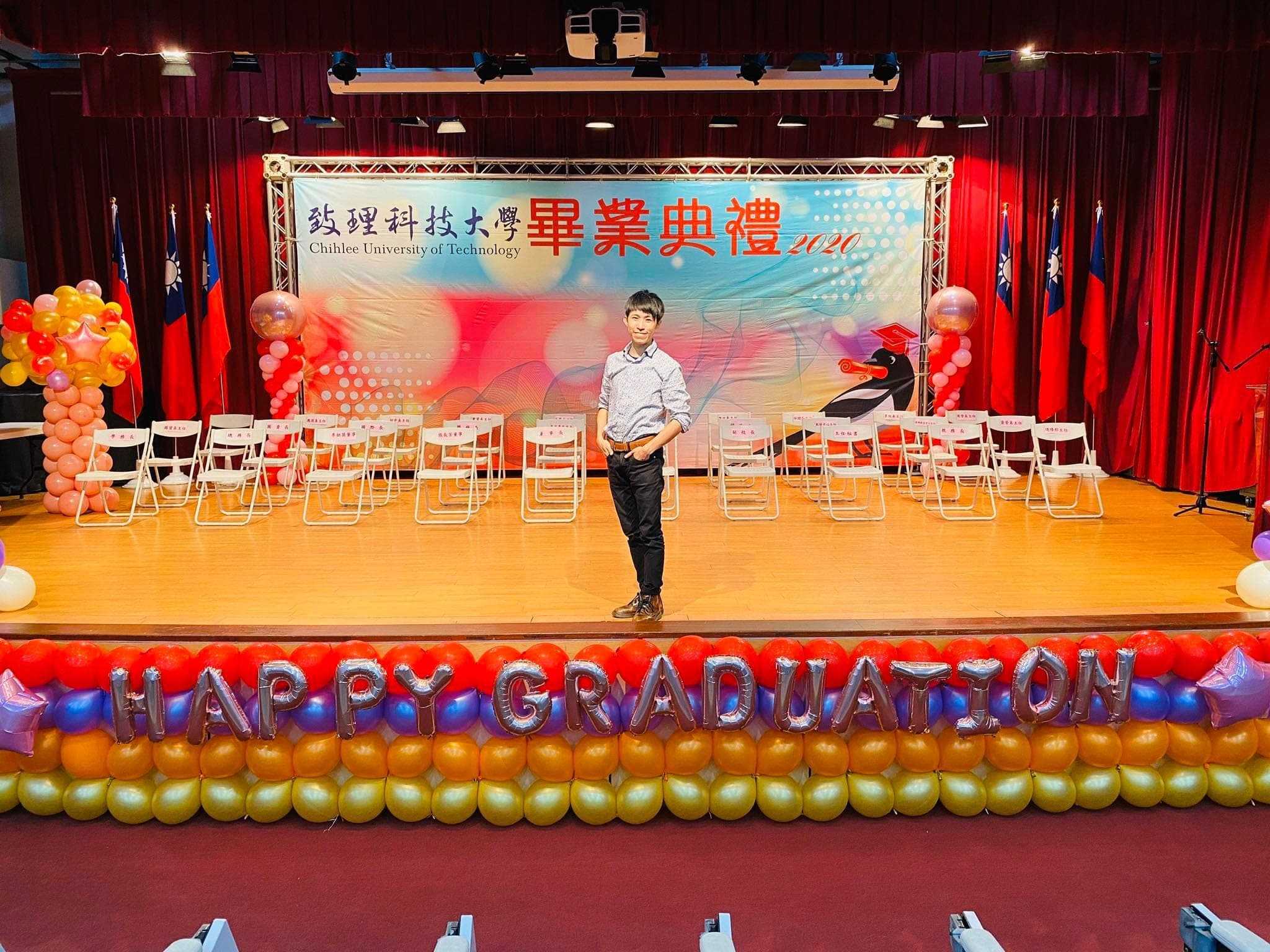 我站在致理科大畢業典禮舞台上,前方是銀色 HAPPY GRADUATION 字母