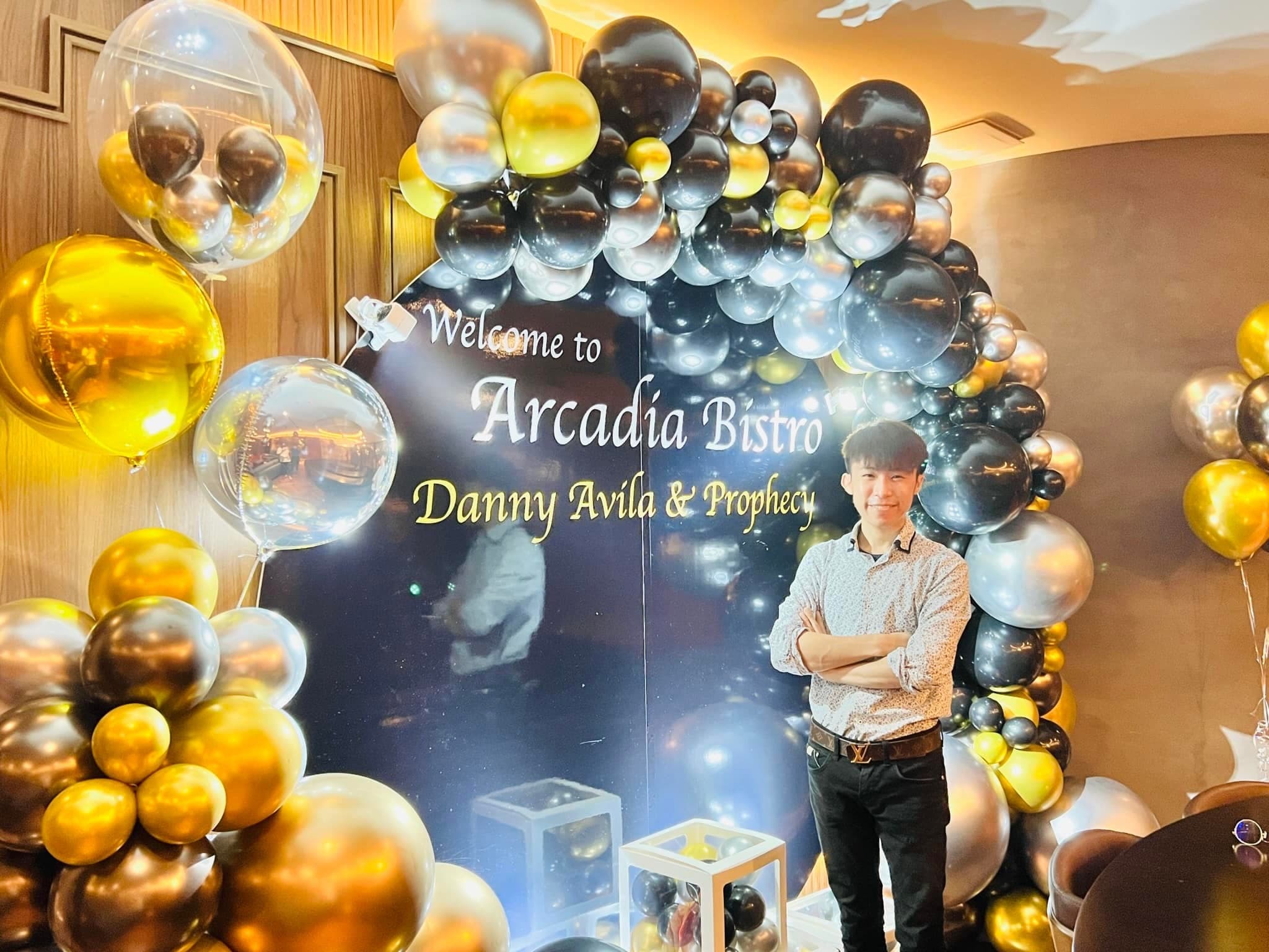 柯男雙手交叉站在黑金銀氣球拱門與星空背板前