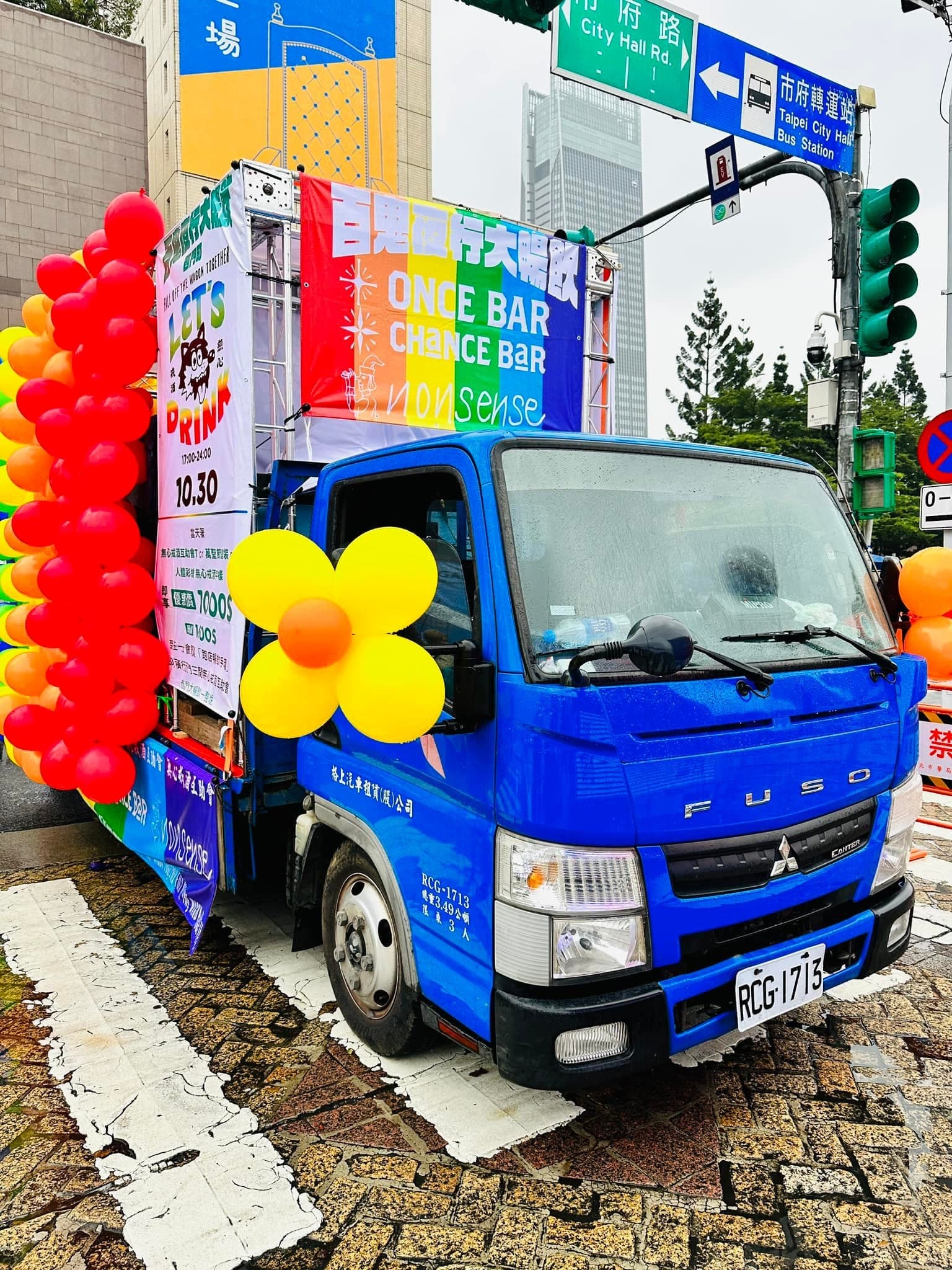 藍色舞台車停在路口,車頭貼著黃橘色的花朵氣球,車身側面是彩虹氣球