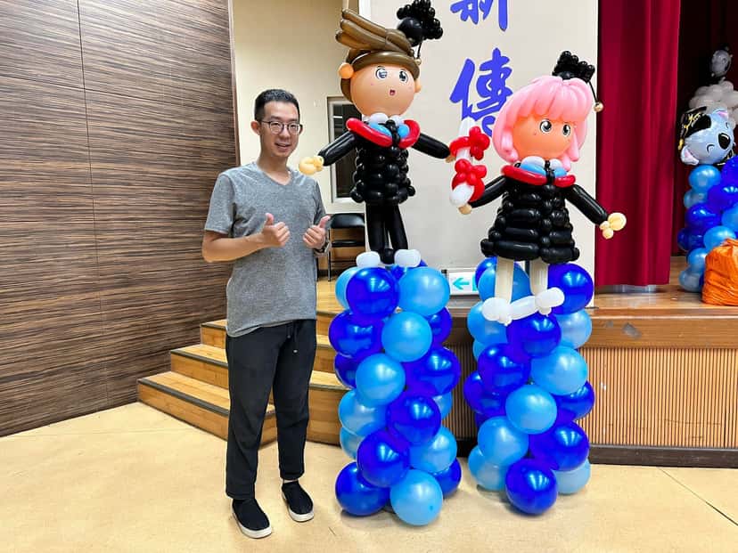 粉紅頭髮的安妮亞與戴學士帽男生畢業人偶,站在深淺藍氣球柱上