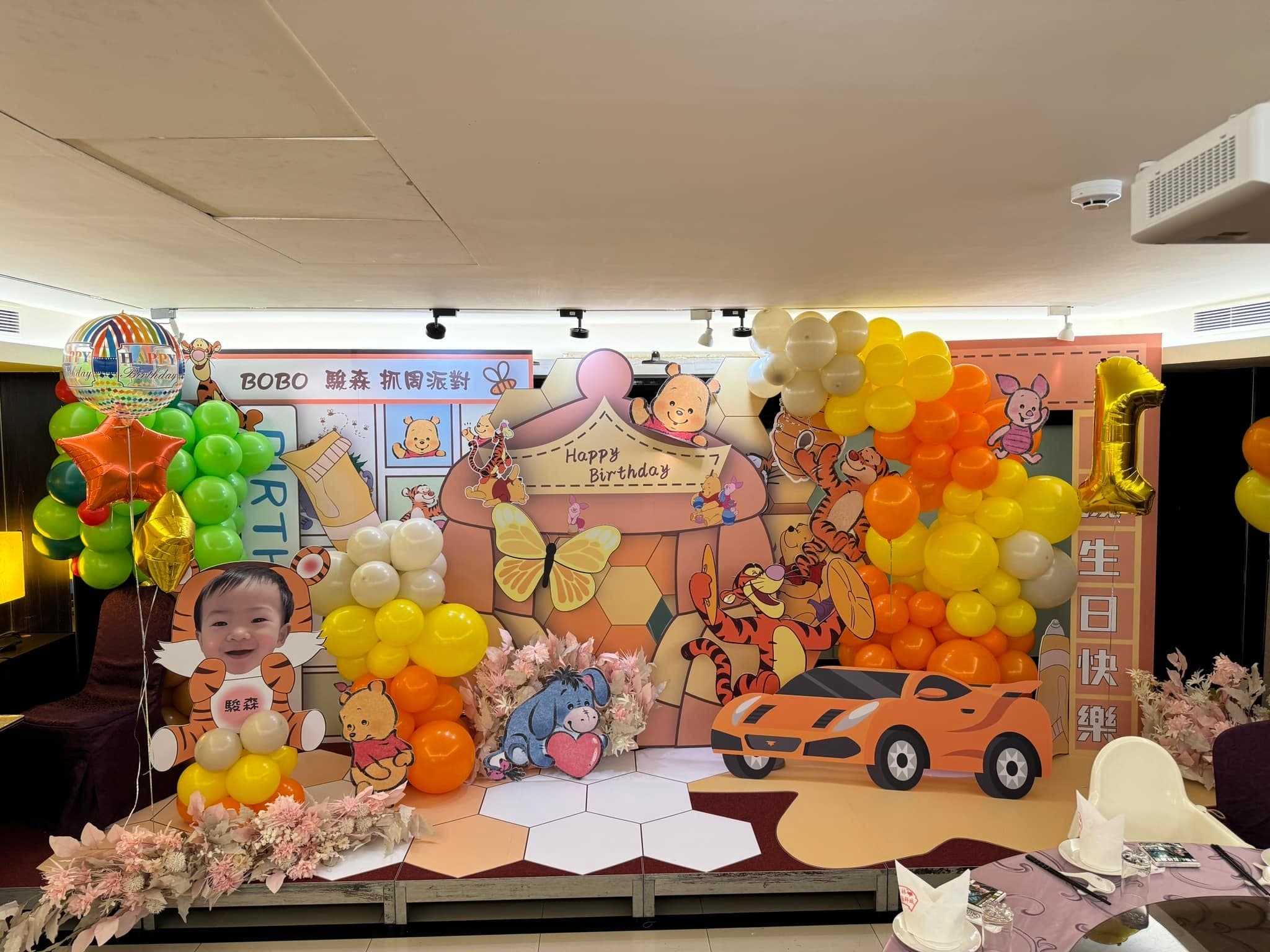新北餐廳的小熊維尼抓周佈置舞台全景,橘黃氣球串與角色立牌