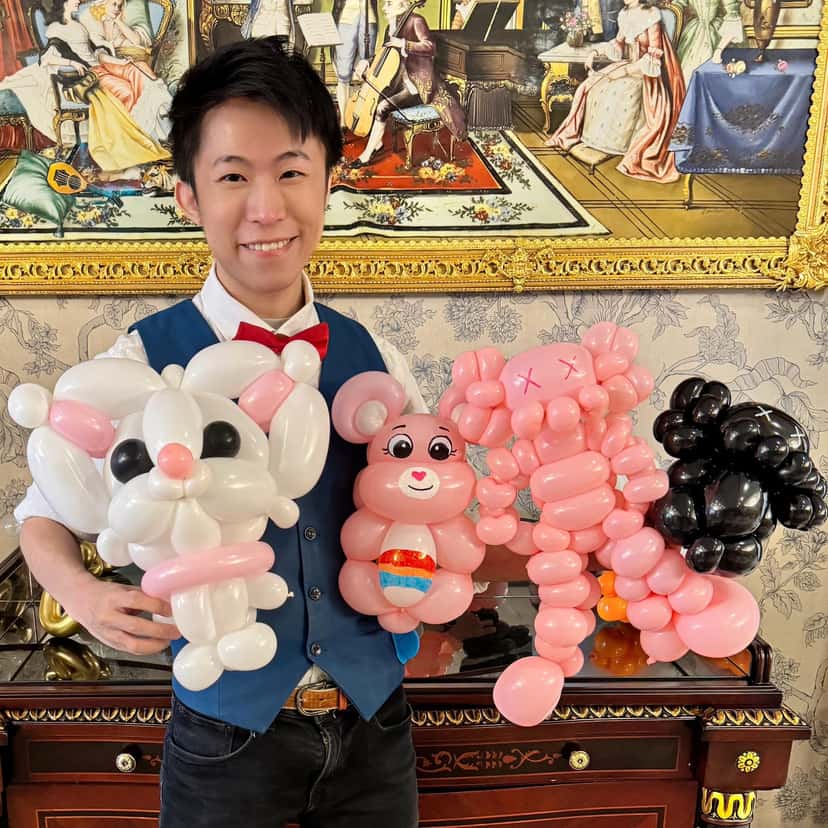 柯男在生日派對會場抱著白貓、彩虹熊、粉紅與黑色 Kaws 公仔造型氣球