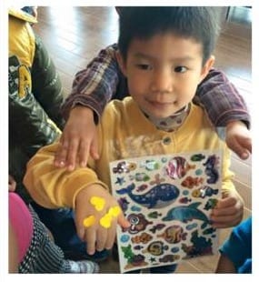 小男孩拿著海洋動物貼紙本,手上也貼著黃色貼紙