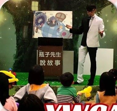 YWCA 故事屋舞台上，柯男穿黑白裝在瓶子先生說故事講台旁講《糖果屋》