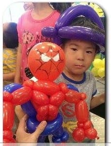 小男孩戴紫色氣球帽、拿紅色蜘蛛人造型氣球