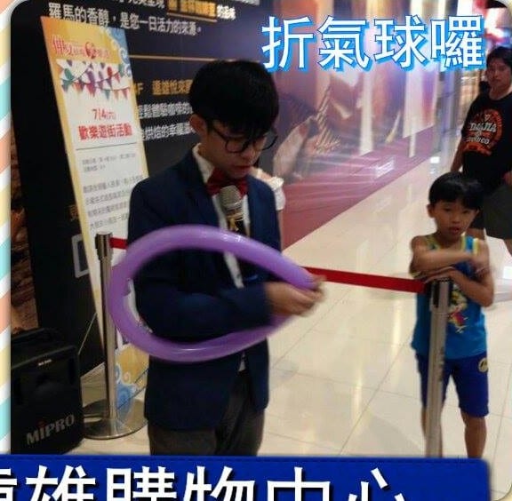 穿藍色西裝的柯男拉著紫色長條氣球折氣球