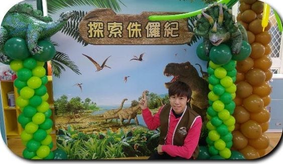 探索侏儸紀恐龍背板，兩側是綠色恐龍與咖啡色棕櫚樹氣球柱