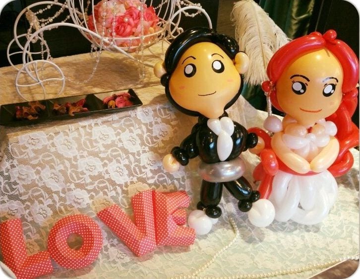 婚禮桌上的新郎新娘氣球人偶，旁邊是紅色 LOVE 字母擺飾