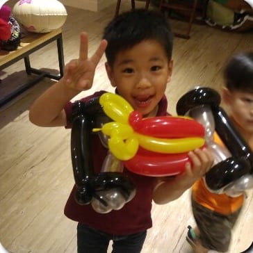 男孩比 YA，抱著紅黃色賽車造型氣球
