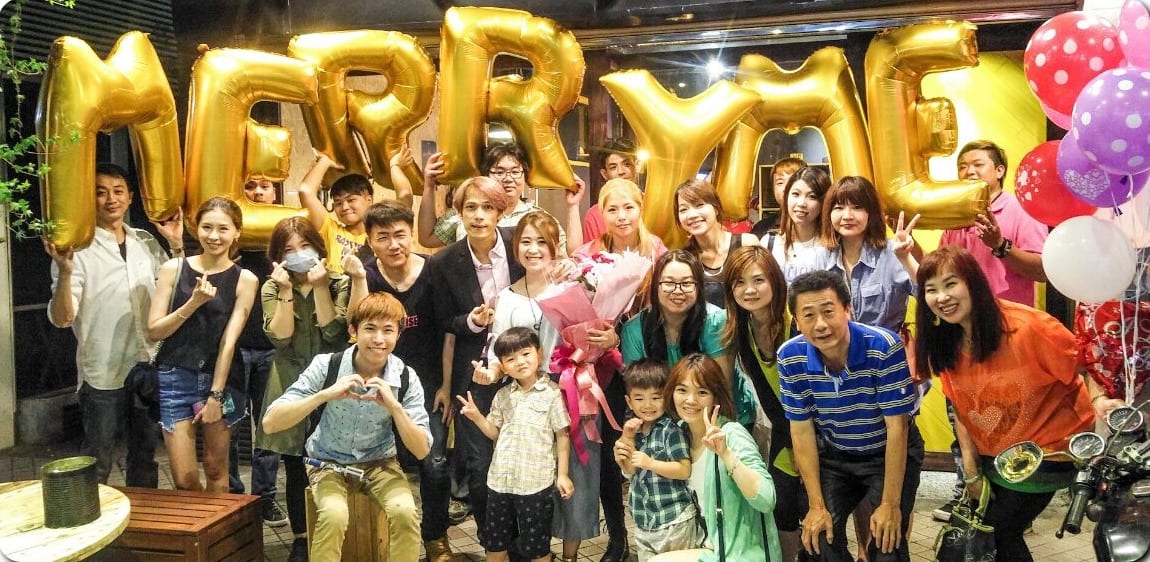 親友舉著金色 MARRY ME 字母氣球，和求婚成功的新人大合照