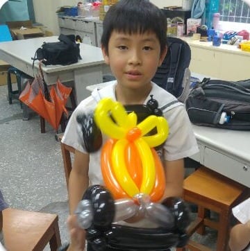 男學生拿著黃橘色蝴蝶結與黑色底座的造型氣球