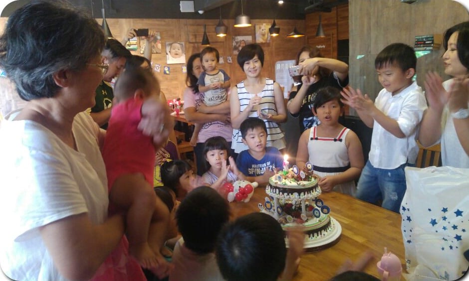 生日派對上大家圍著兩層蛋糕唱生日快樂歌