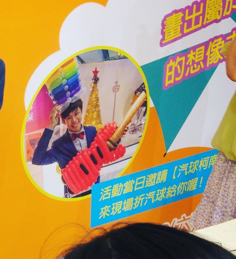 櫃位活動海報上,戴彩虹氣球帽的折氣球表演者照片