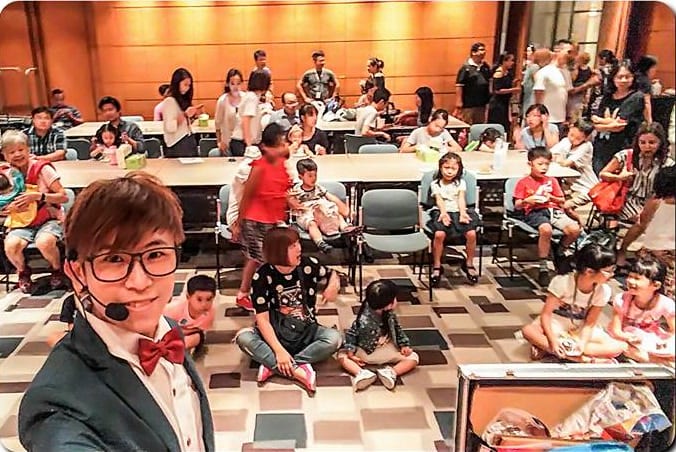 戴耳掛麥克風的我在會議廳前方自拍,後方坐滿親子觀眾