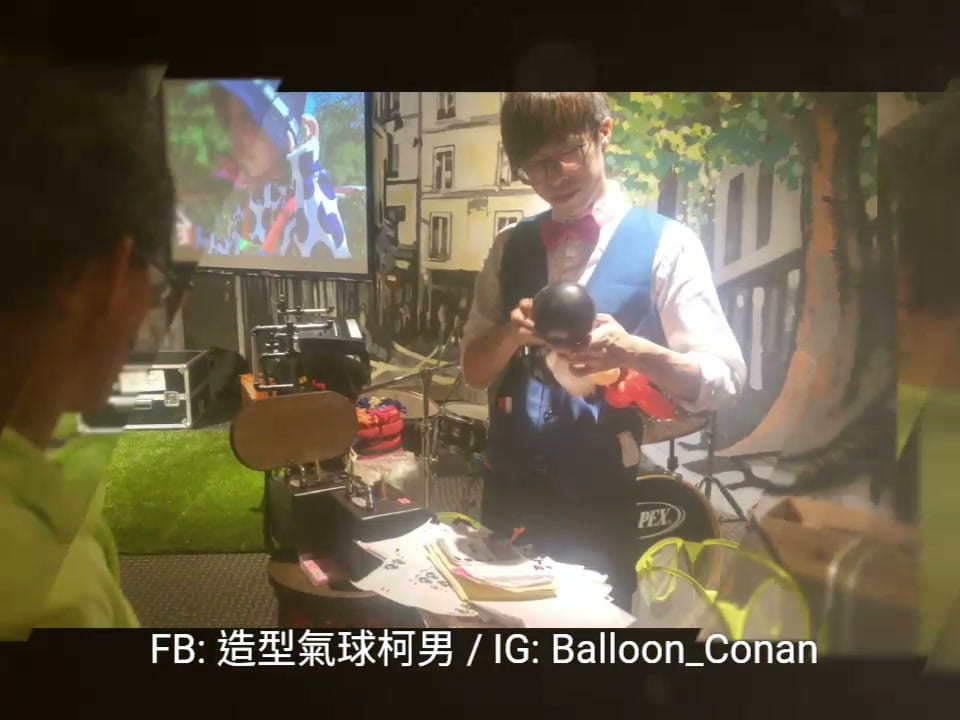 生日派對現場,柯男穿藍背心在餐廳舞台旁折黑色米奇造型氣球