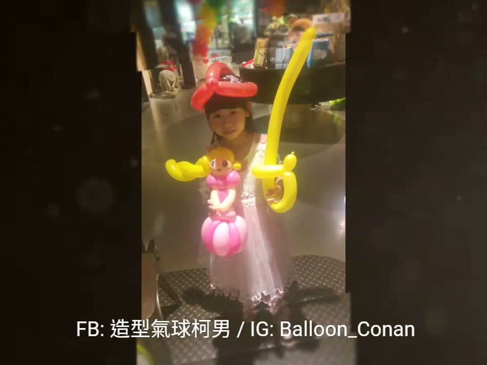 小女孩戴紅色蝴蝶結氣球頭飾,拿著粉紅公主和黃色寶劍造型氣球