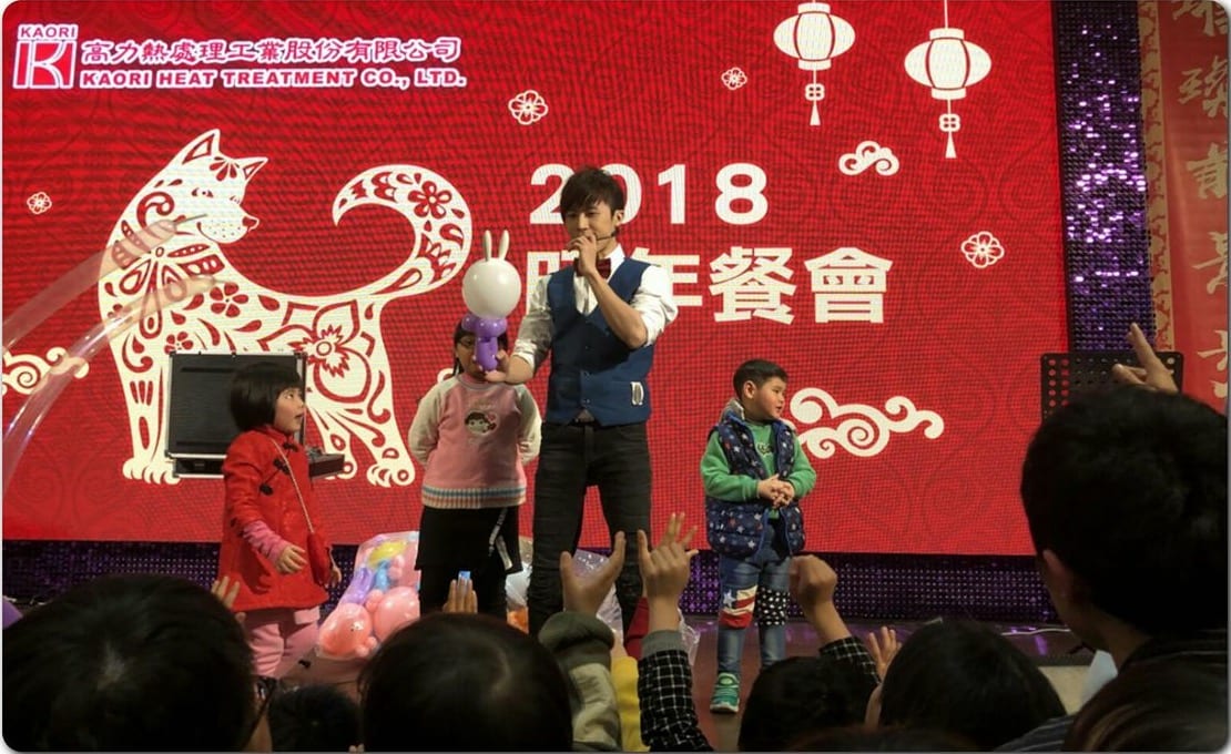 桃園高力熱處理 2018 年終餐會舞台，柯男拿麥克風表演魔術氣球秀，三位小朋友上台互動
