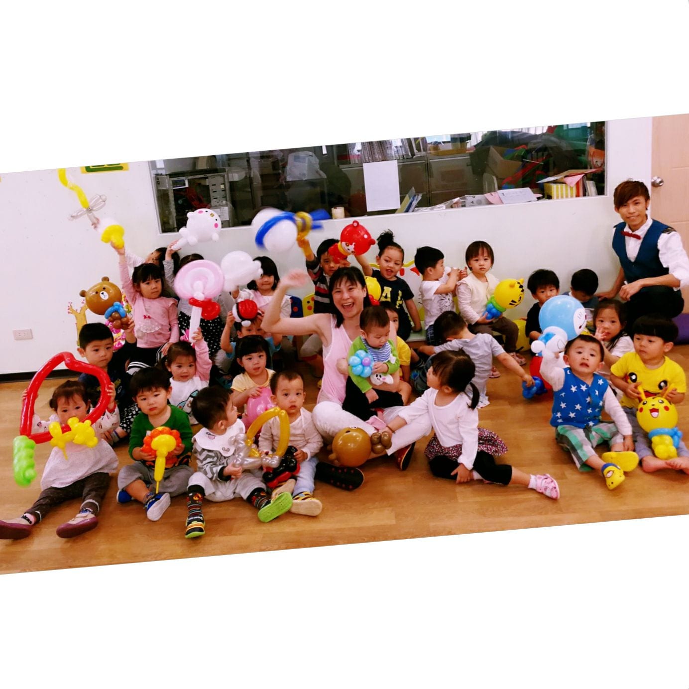 新北板橋快樂森林托嬰中心兒童節，小小孩們坐在木地板上拿著巧虎、熊大、皮卡丘造型氣球大合照