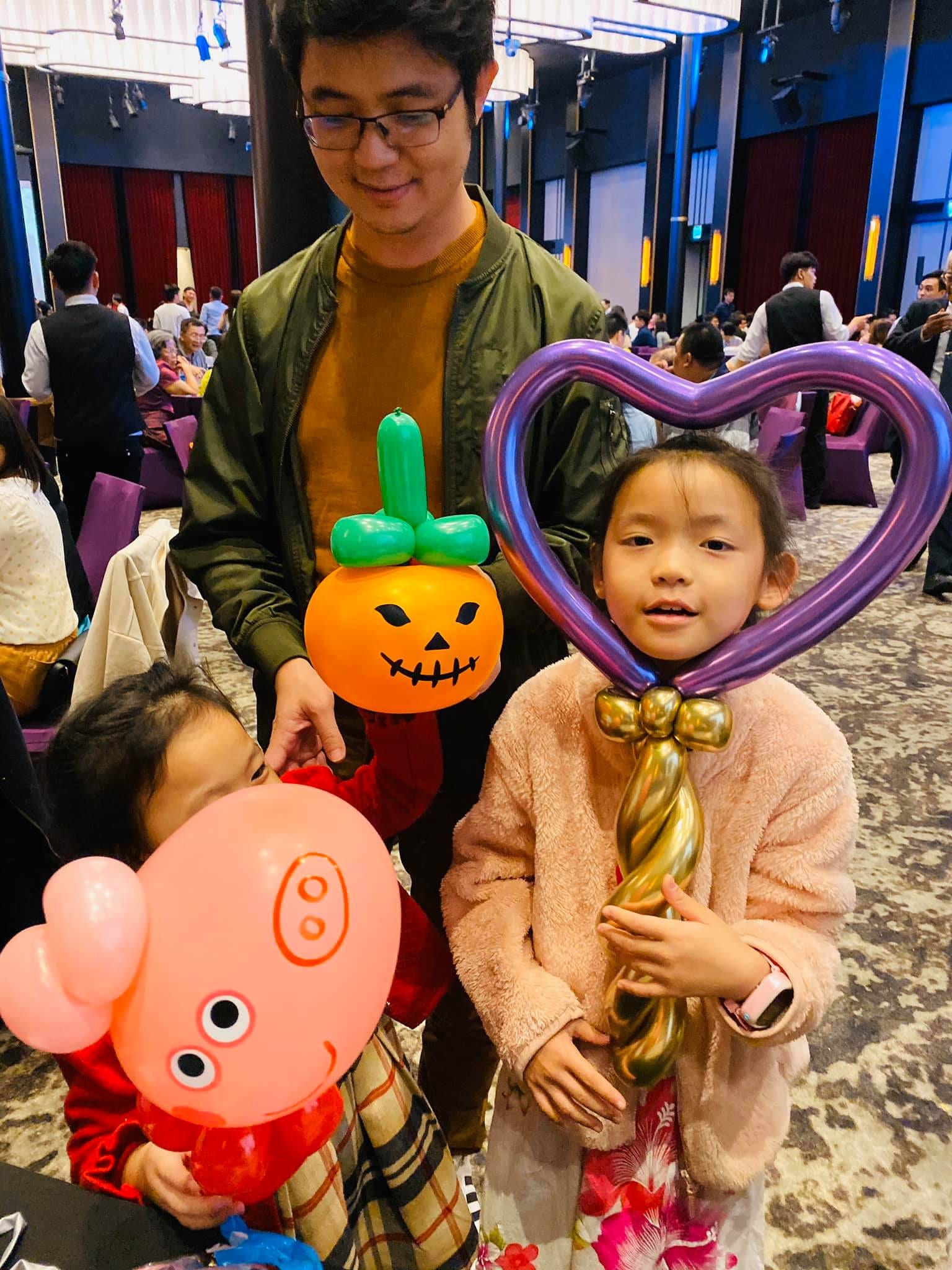 女孩拿紫色愛心魔法棒氣球，旁邊有南瓜和粉紅小豬造型氣球