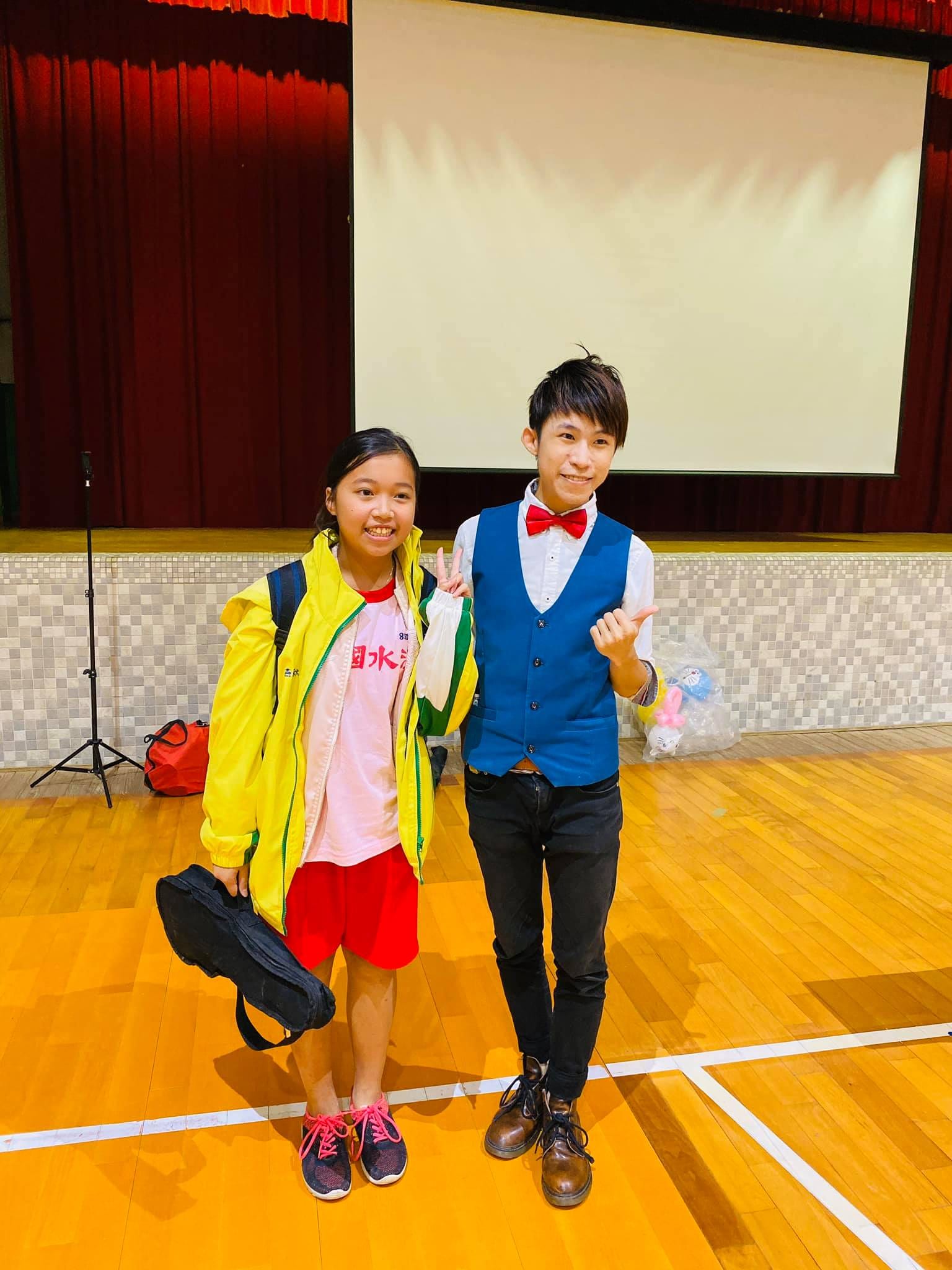 穿黃綠色外套的女同學和講者在體育館舞台前比手勢合照