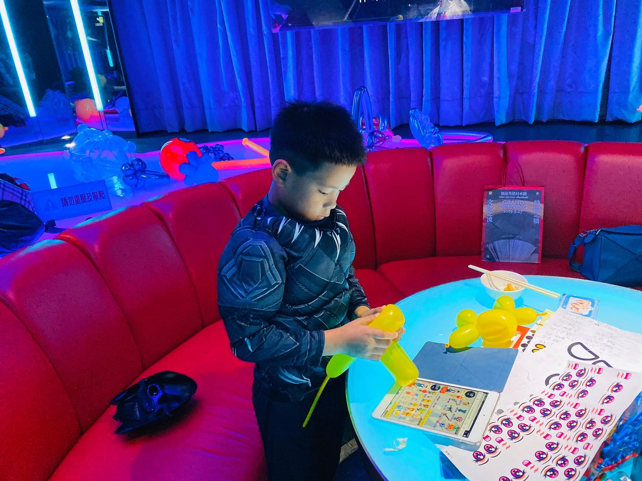 穿黑豹服裝的男孩在包廂桌邊自己折黃色貴賓狗