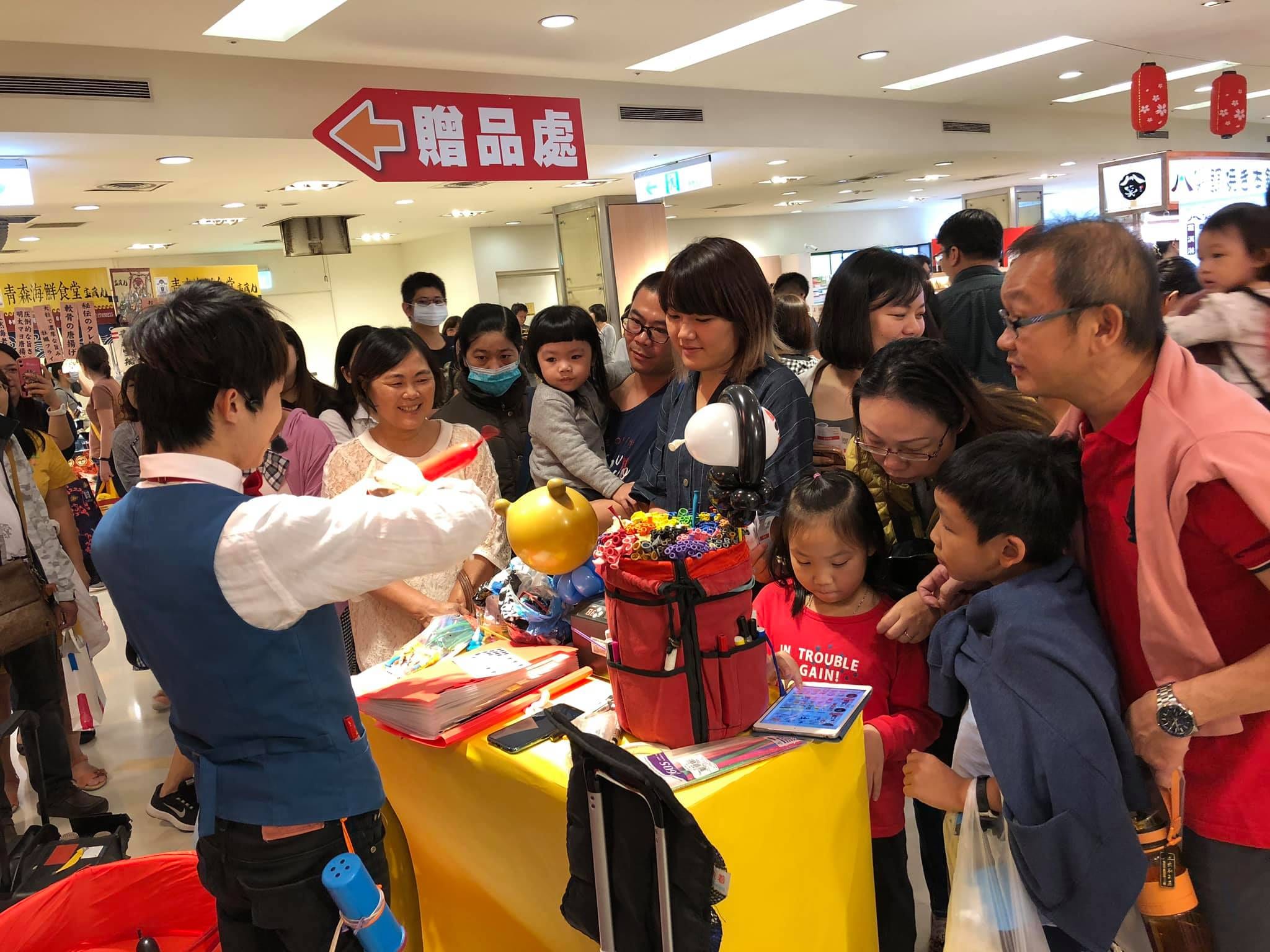 日本展贈品處旁的黃色折氣球桌,我邊折邊和排隊的家庭說話