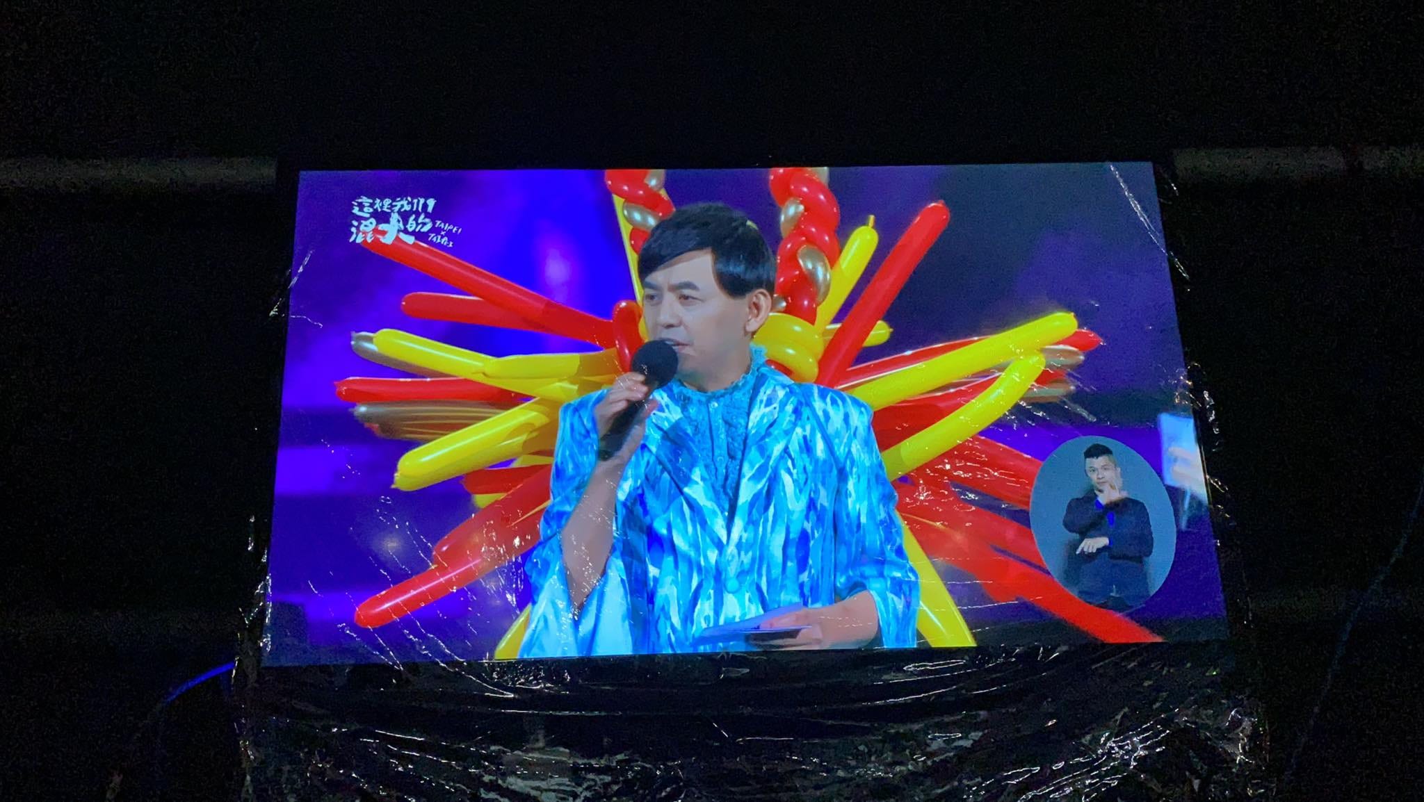 螢幕轉播黃子佼藍色亮片裝與身後放射狀紅黃氣球