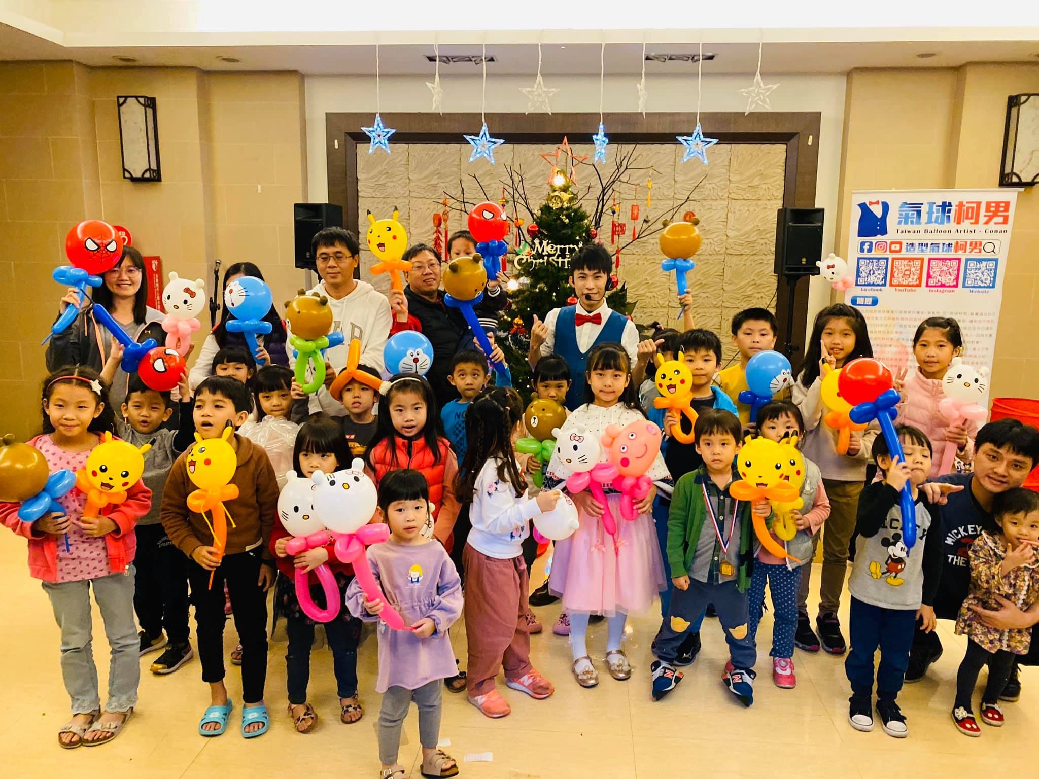 土城社區聖誕樹前的大合照，孩子們舉著皮卡丘、Hello Kitty、哆啦A夢等氣球手持棒