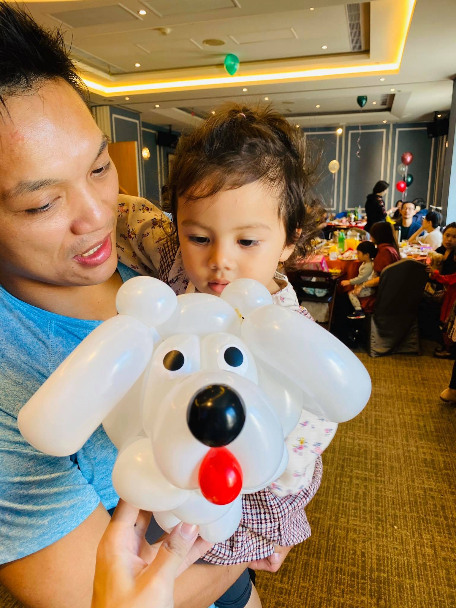 爸爸抱著幼兒，前面是吐紅舌頭的白色小狗造型氣球