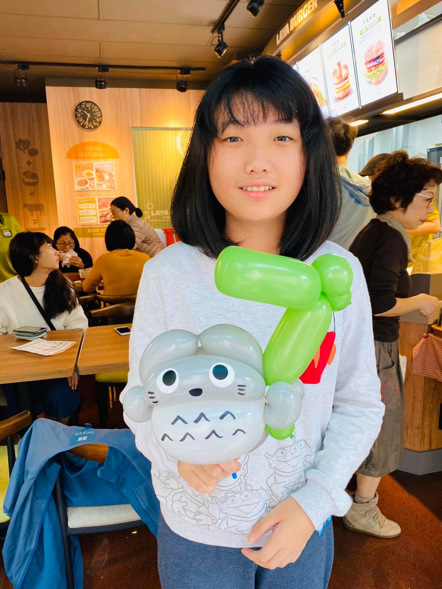 店內用餐區，女孩拿著灰色龍貓與綠色葉子造型氣球