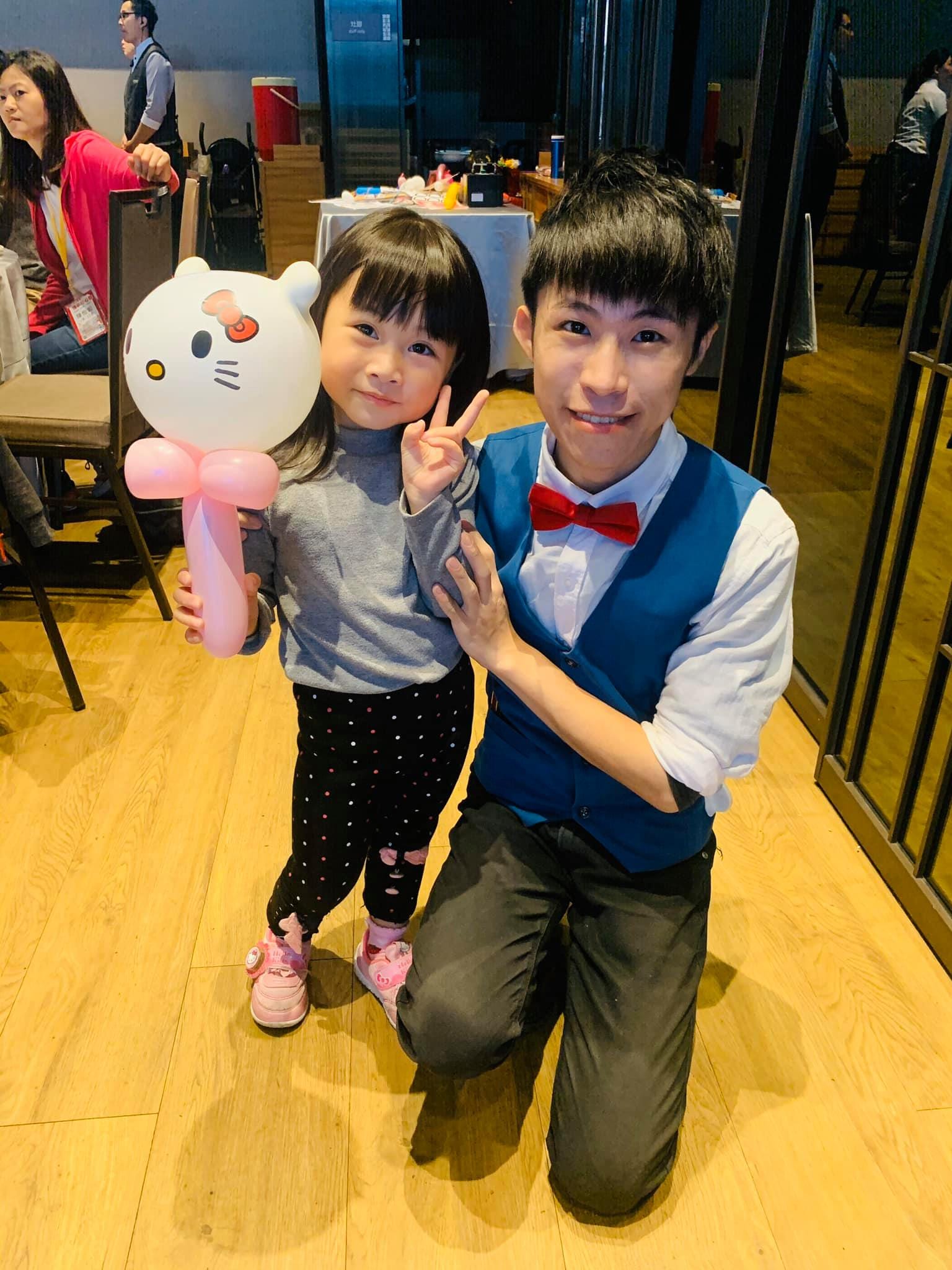 比 YA 的小女孩拿著 Hello Kitty 造型氣球，我蹲在旁邊合照