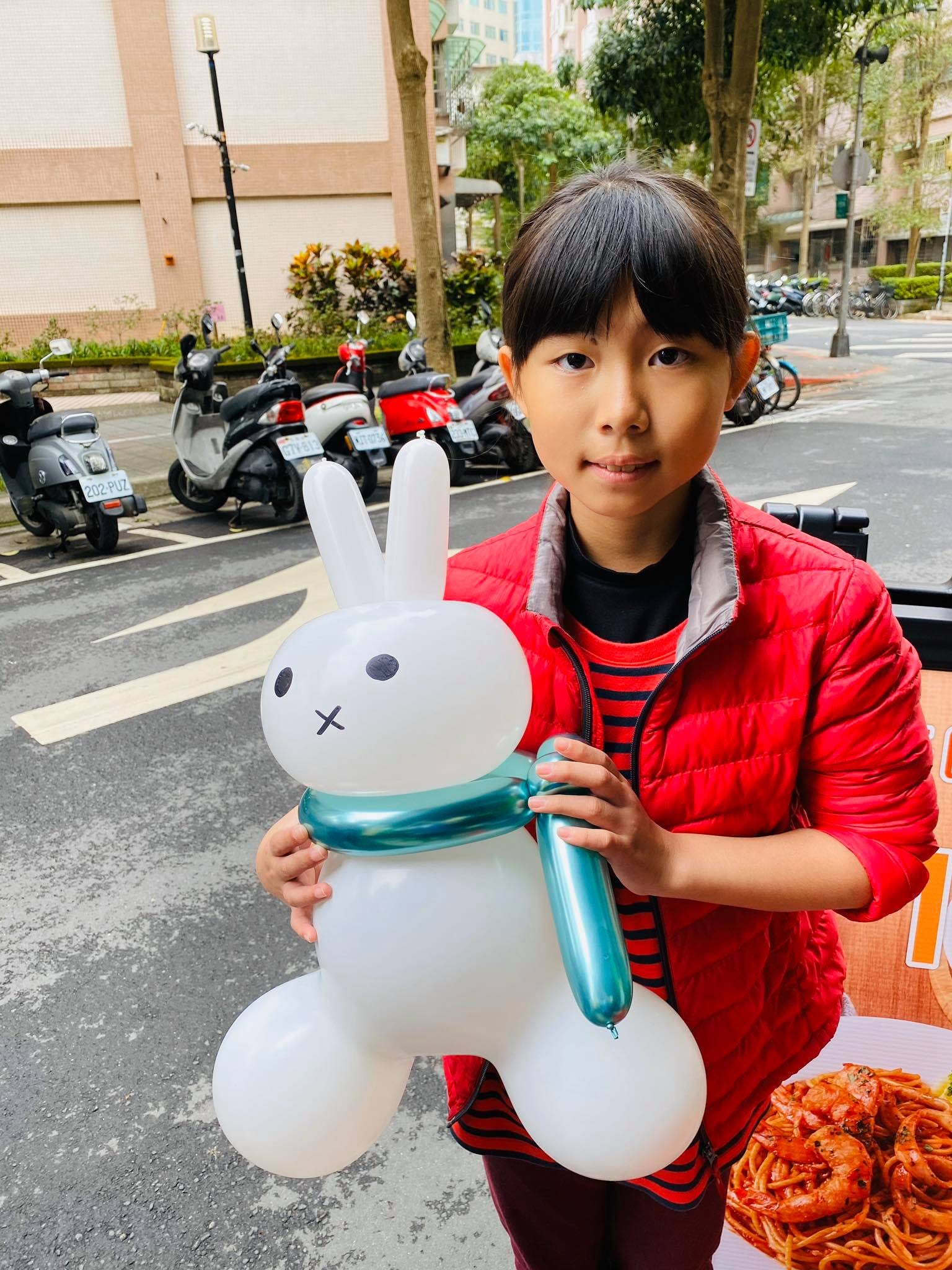 穿紅色外套的女孩抱著圍湖水綠圍巾的白色兔子氣球