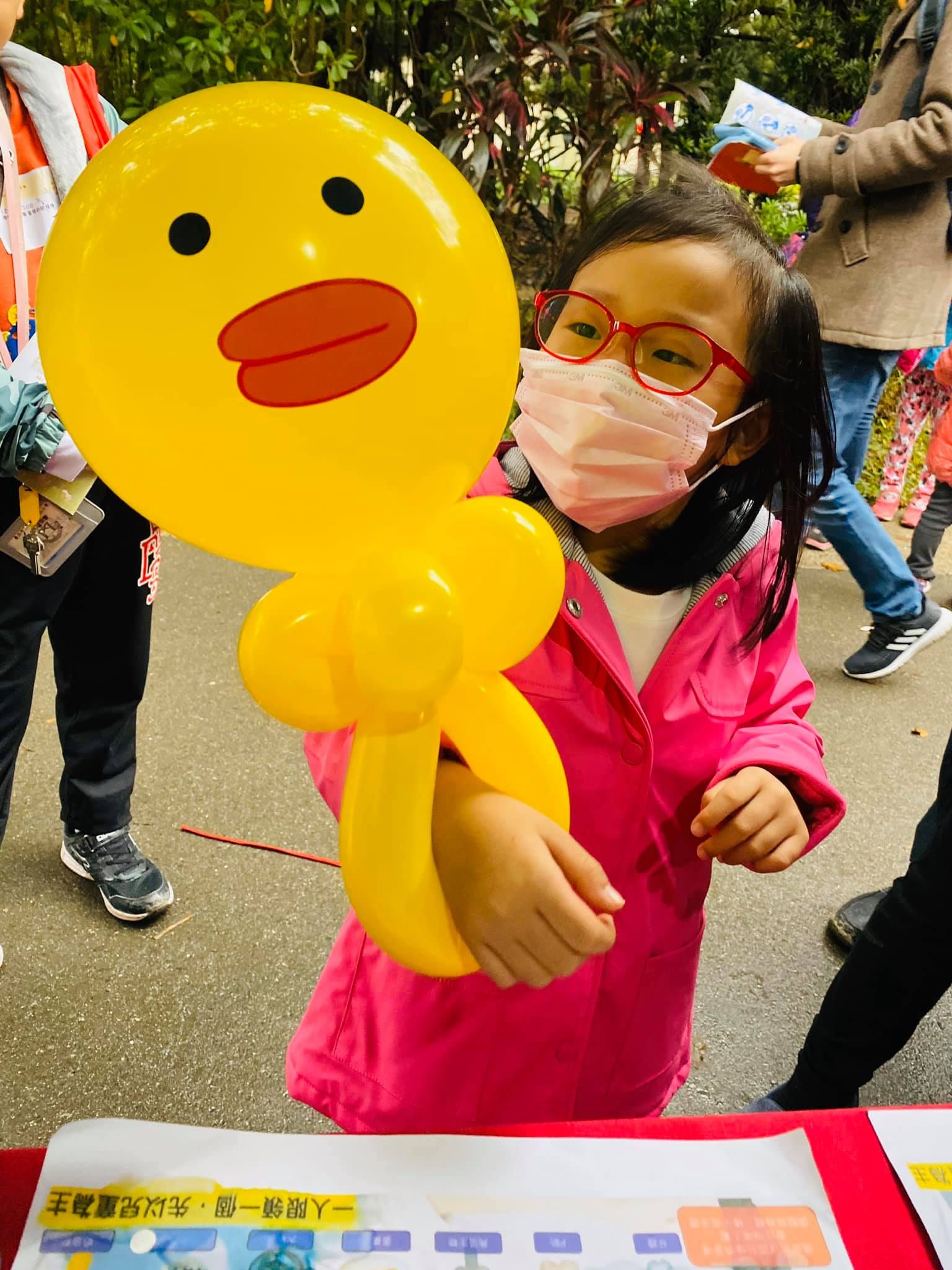 戴口罩的女孩舉起黃色莎莉鴨造型氣球