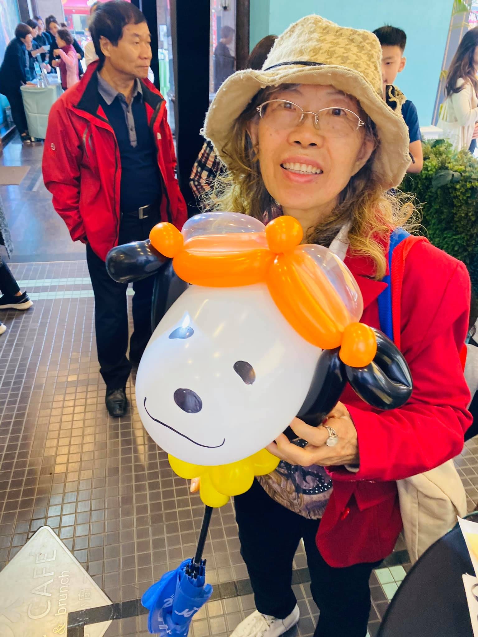 戴漁夫帽的阿姨抱著戴橘色帽子的白色小狗大型氣球