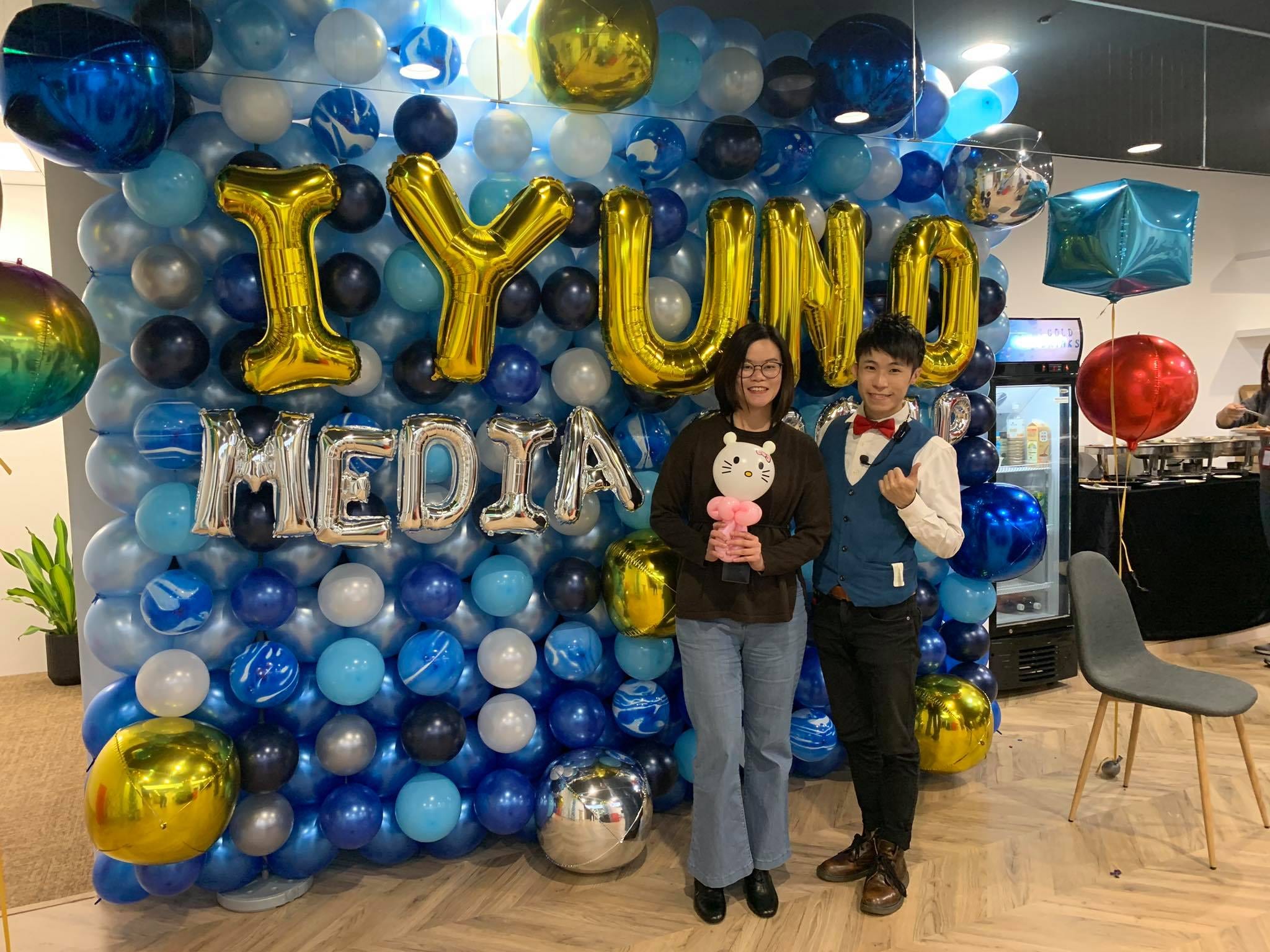 來賓抱著白色小熊造型氣球，和我在 IYUNO 氣球牆前合照