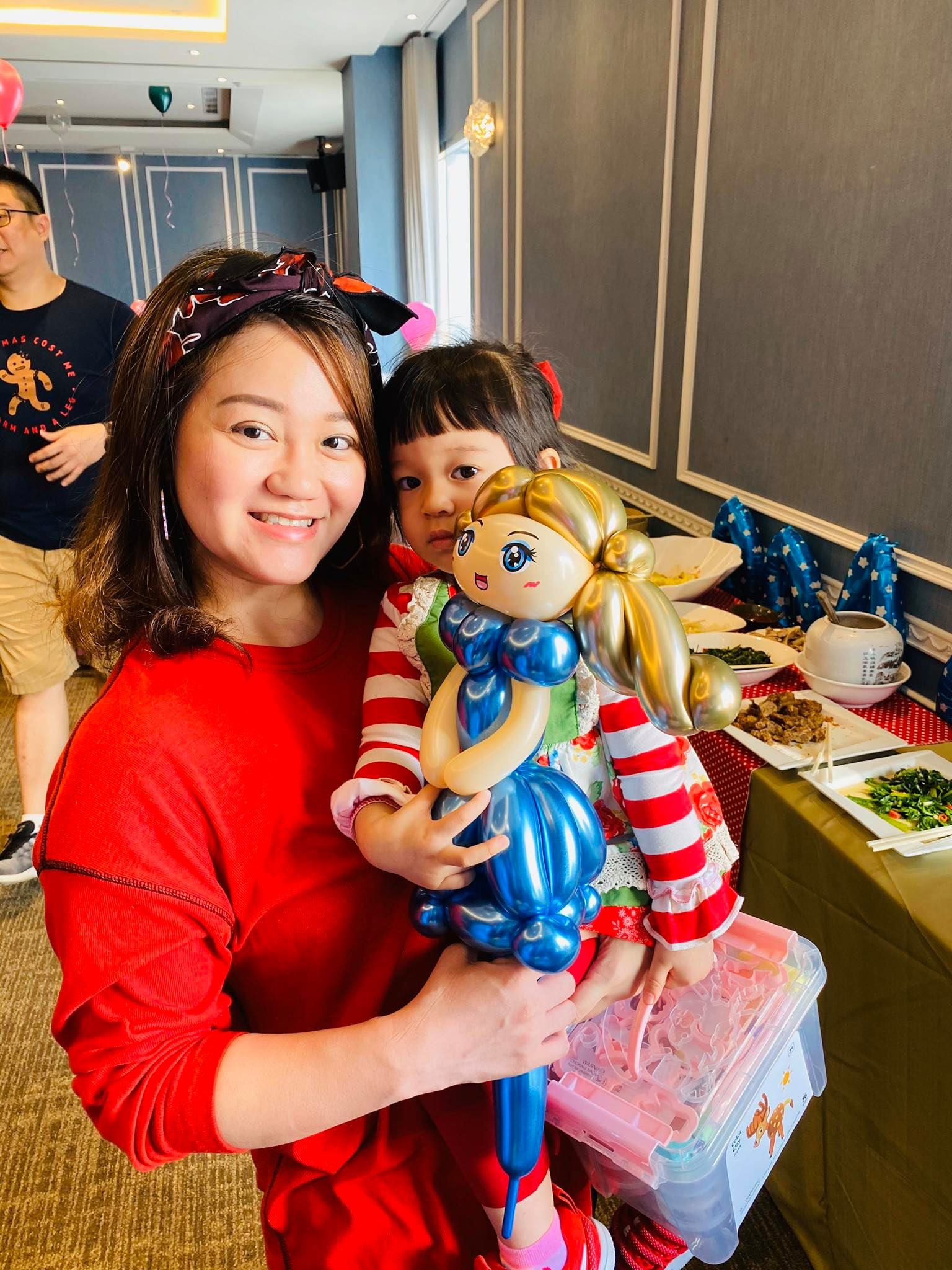 媽媽抱著女兒，拿著金髮雙馬尾、藍洋裝的女孩造型氣球
