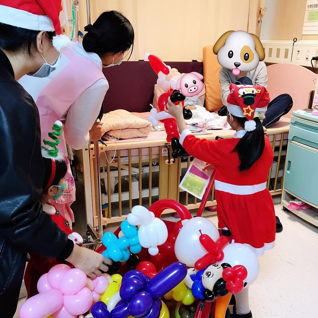 護理師陪同下，聖誕裝女孩把白色與粉紅色氣球送到嬰兒床邊