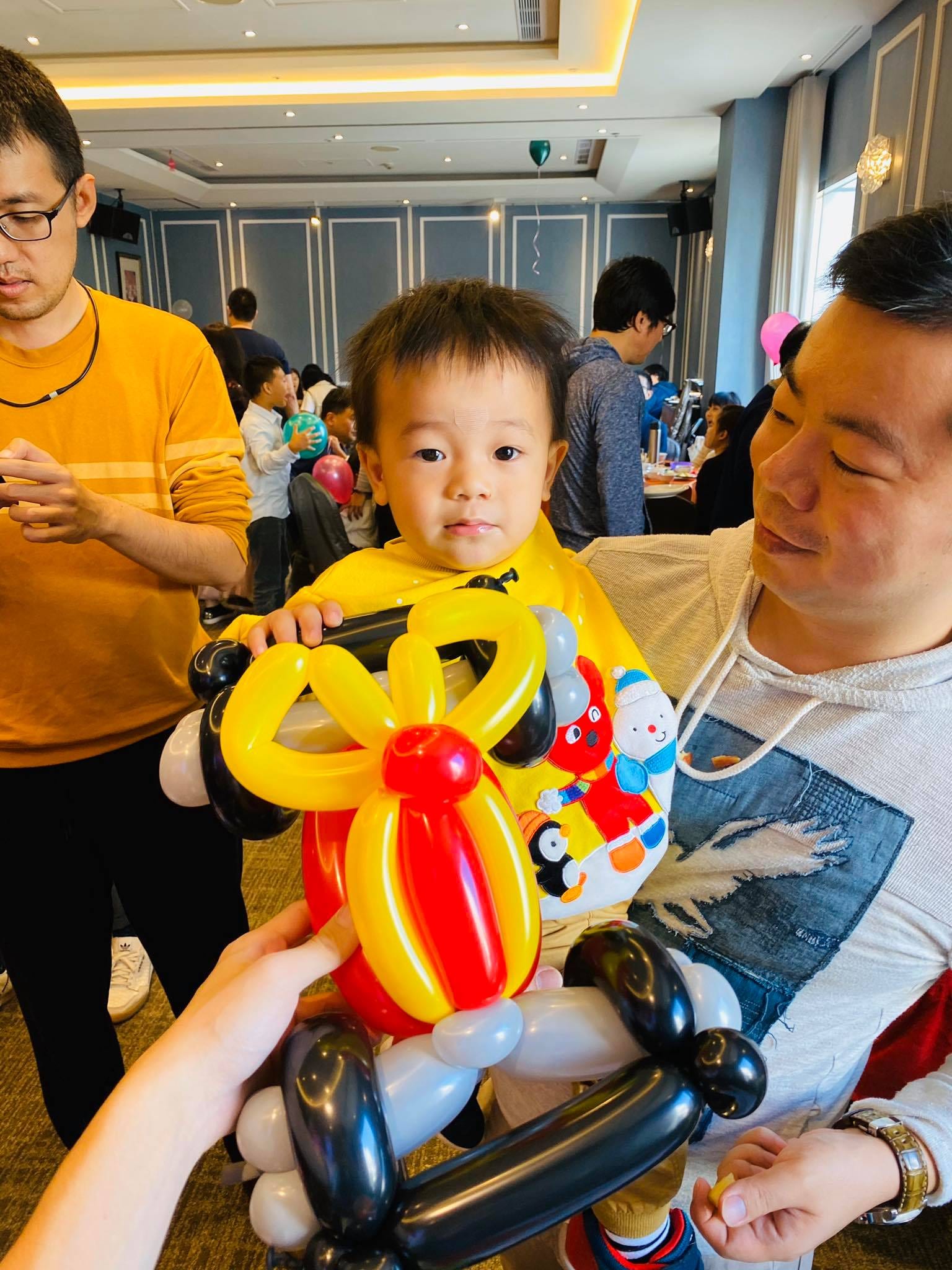 小男孩抱著紅黃色、黑色輪子的交通工具造型氣球