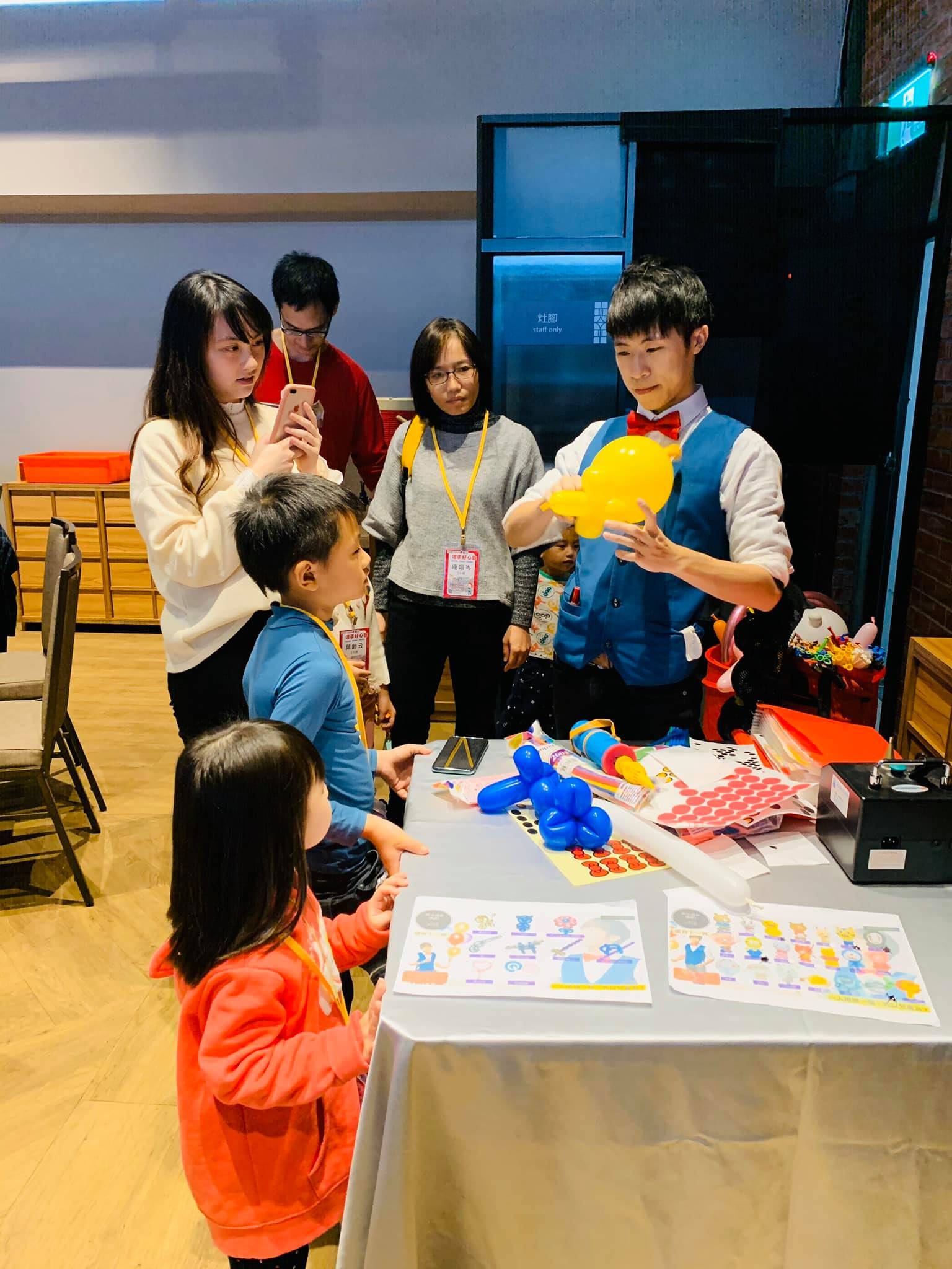 我在折氣球桌前邊折邊和孩子說話，家長與小朋友圍在旁邊