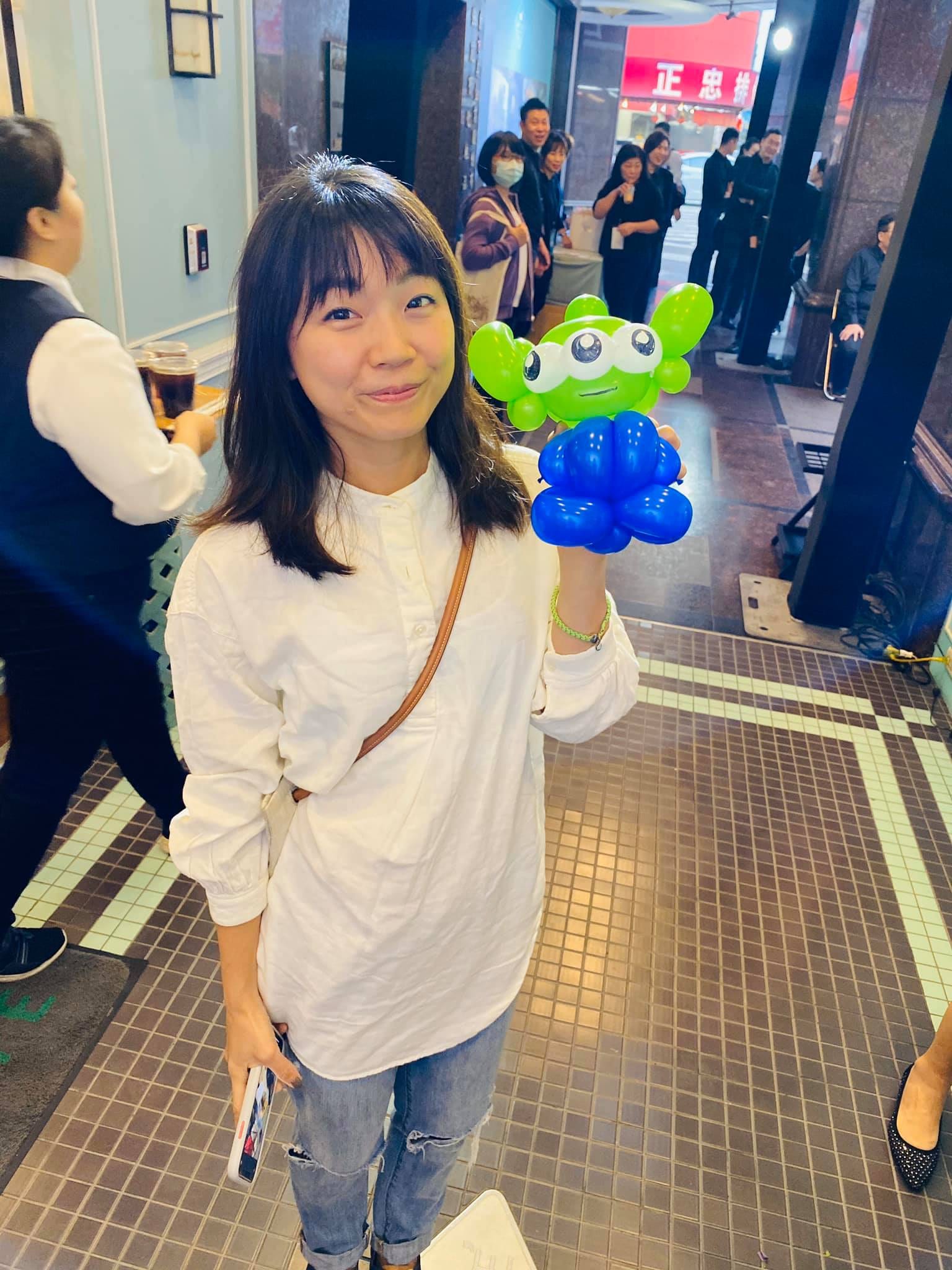 穿白上衣的女生舉起綠色三眼怪造型氣球