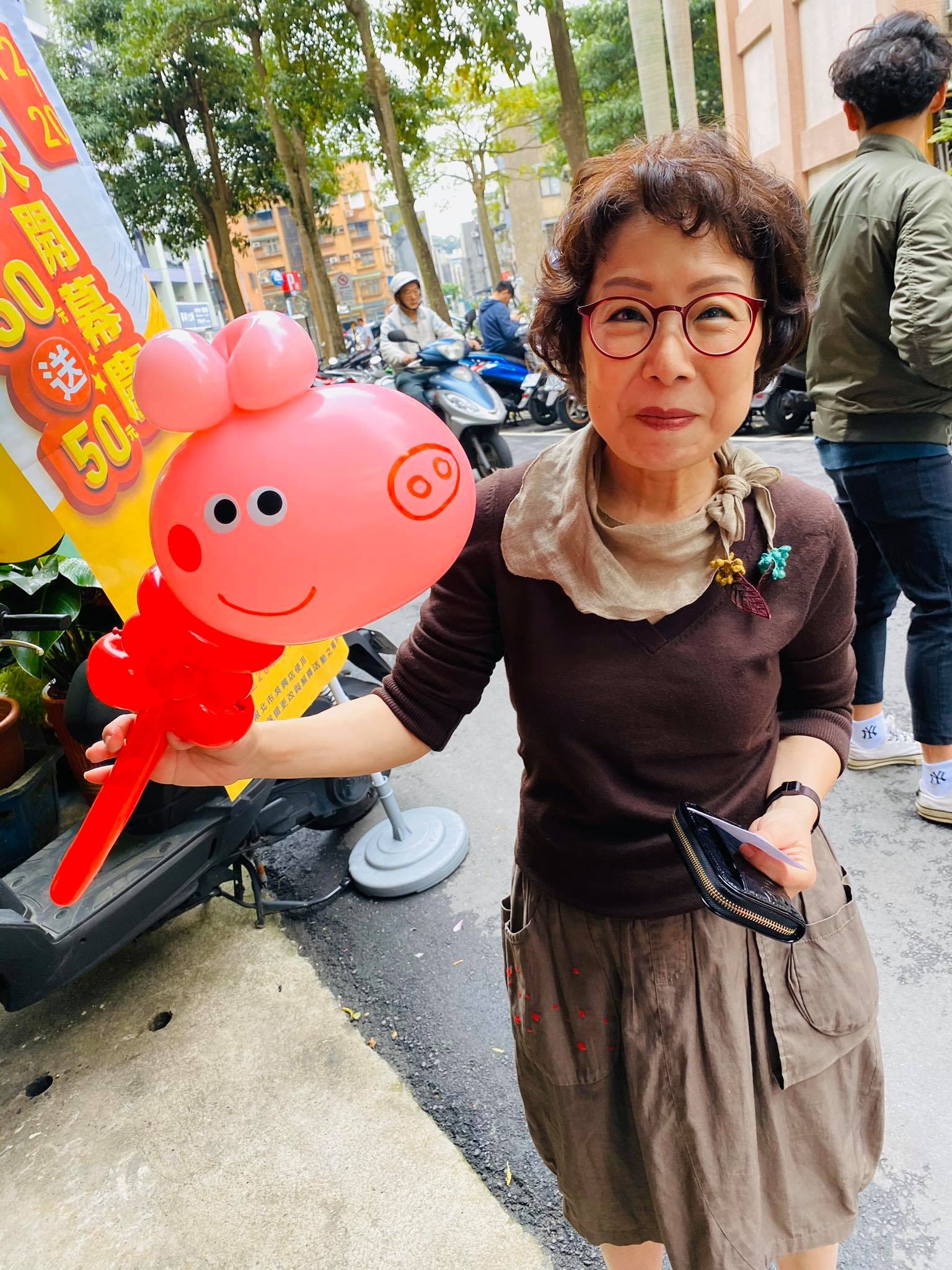 戴眼鏡的女士在門市外拿著粉紅色佩佩豬造型手拿棒
