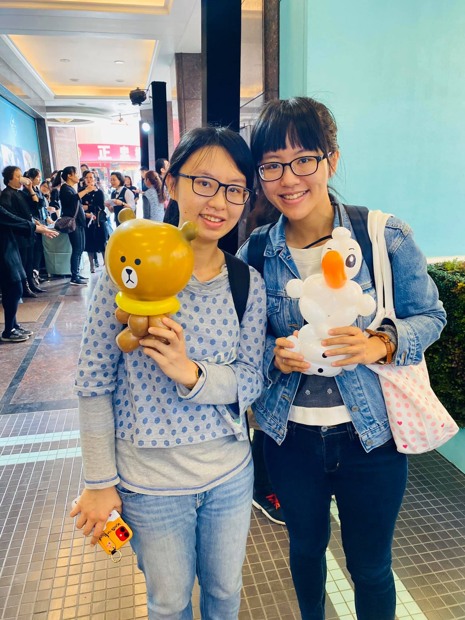 兩位女生分別拿著咖啡色小熊與白色小鴨氣球
