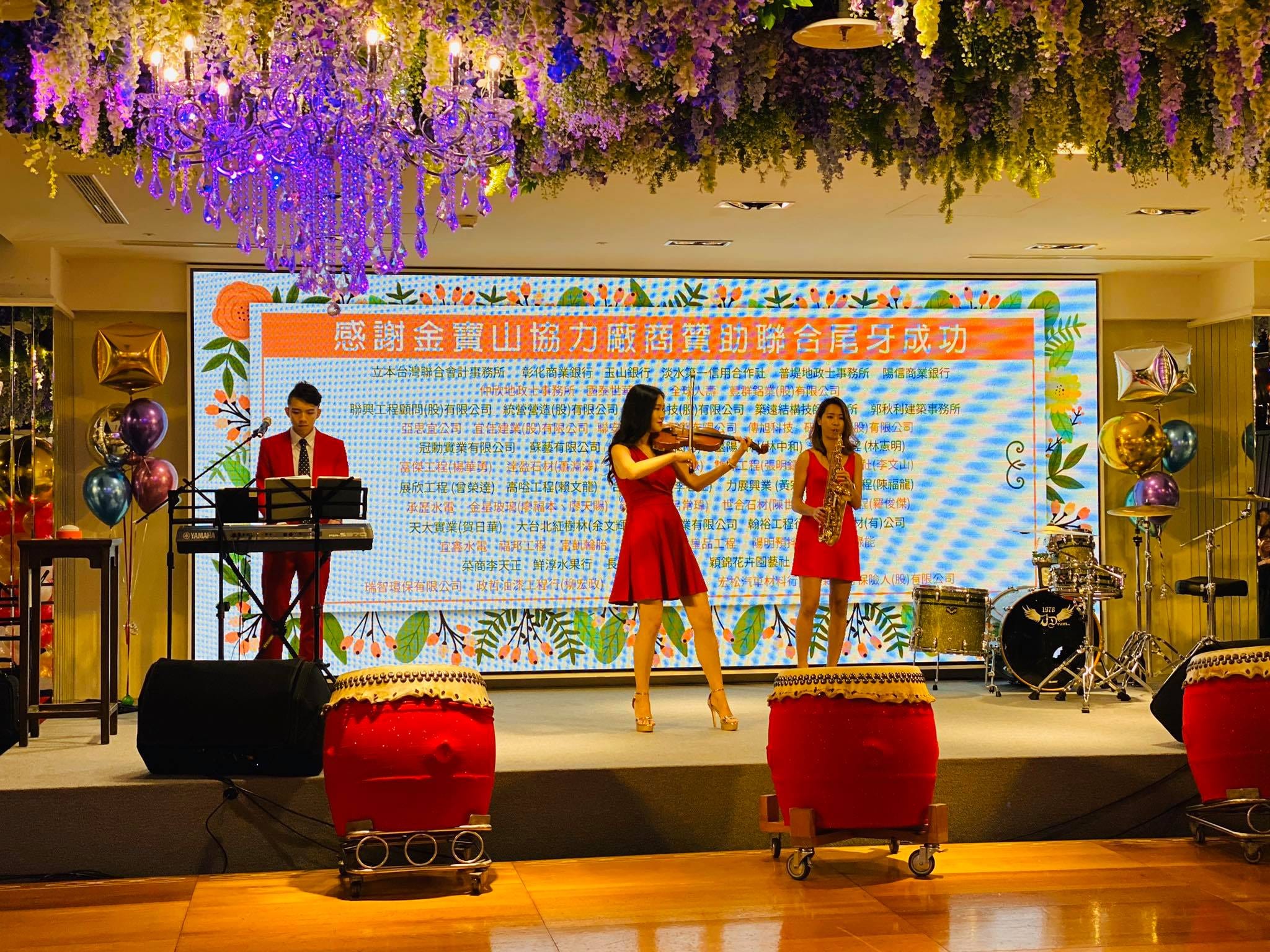 紫藤花裝飾的舞台上，紅衣樂手拉小提琴與吹薩克斯風