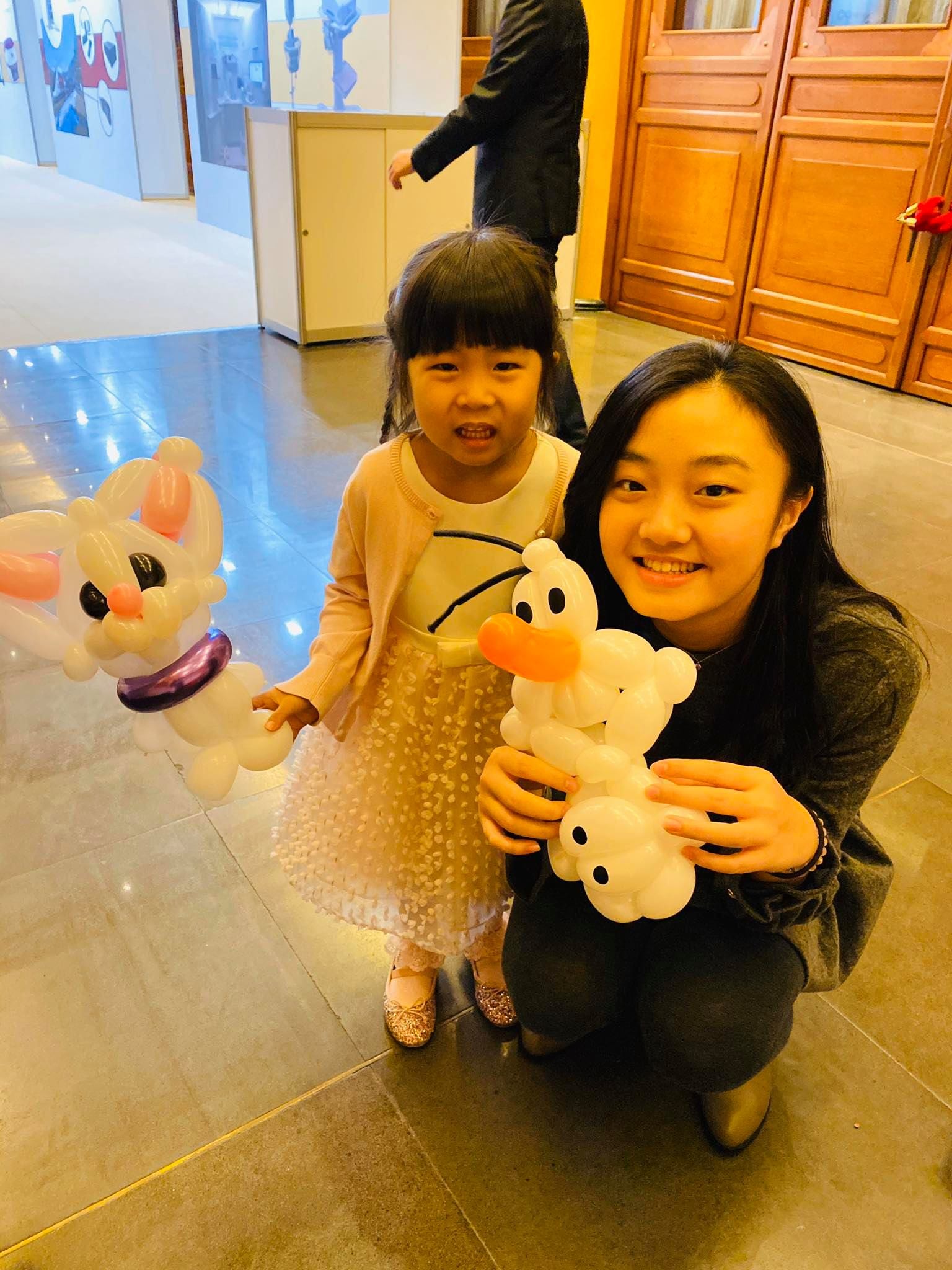 小女孩和姊姊分別拿著白色小貓與橘鼻子雪人氣球
