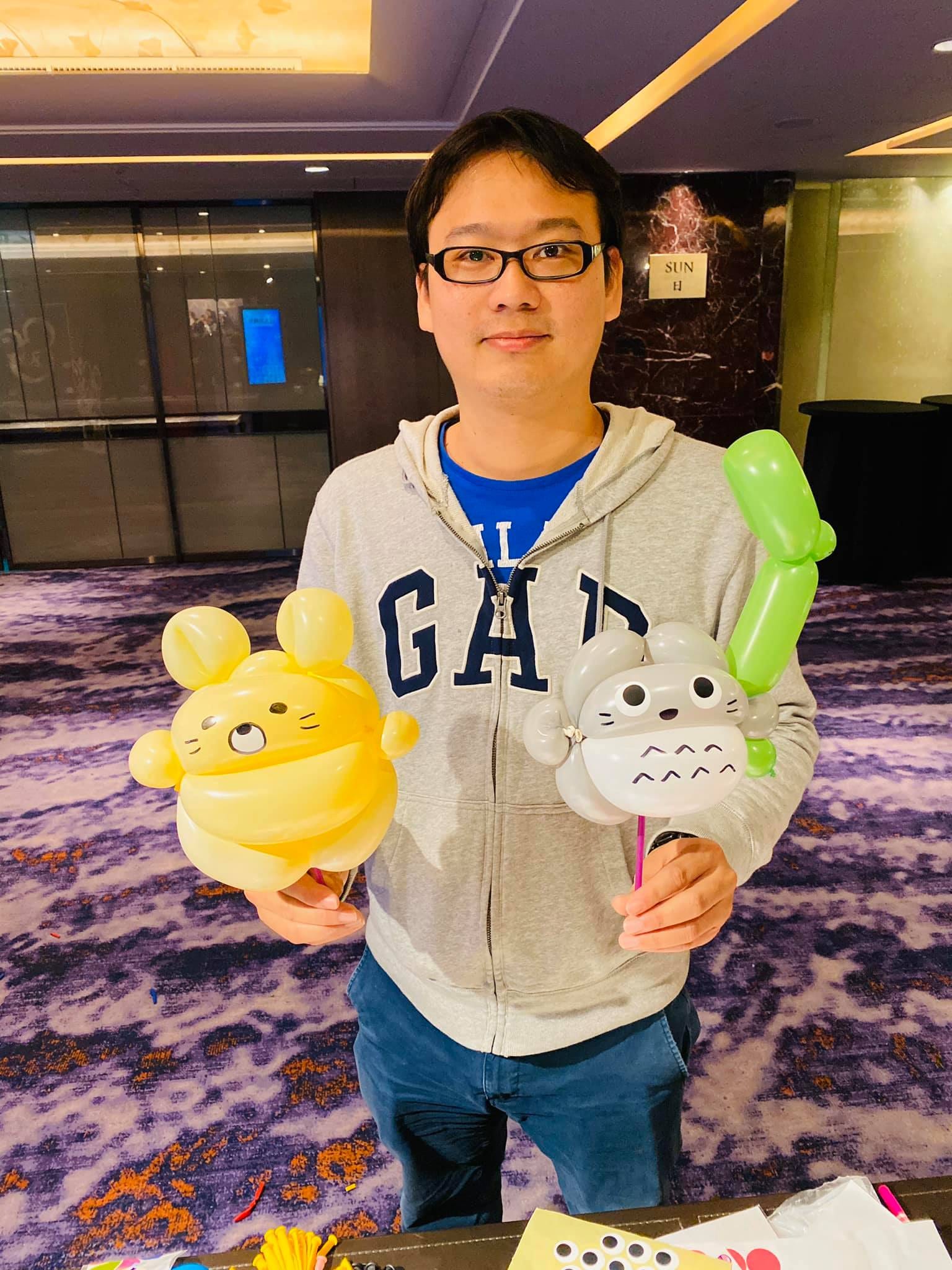 穿灰色連帽外套的男士拿著黃色小熊與灰色龍貓氣球