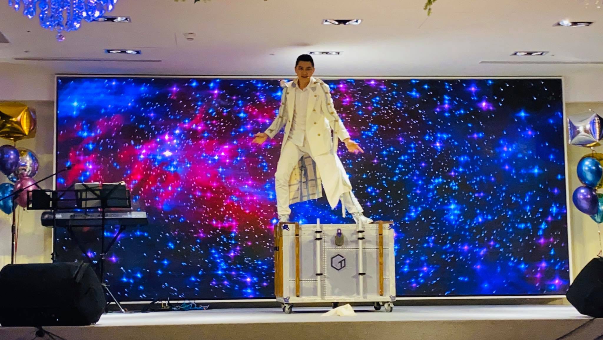 魔術師站在星空背景的舞台上，腳下是銀色大道具箱