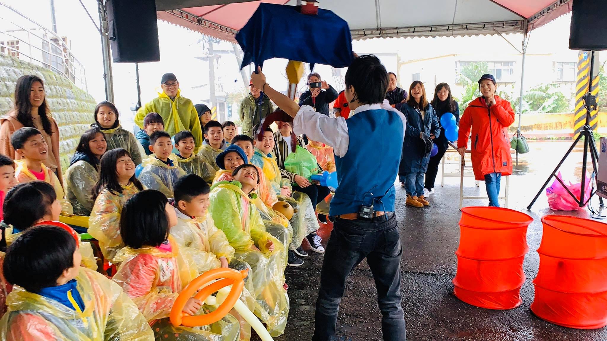 我在帳篷下舉起藍色布巾表演魔術，前排小朋友抬頭看
