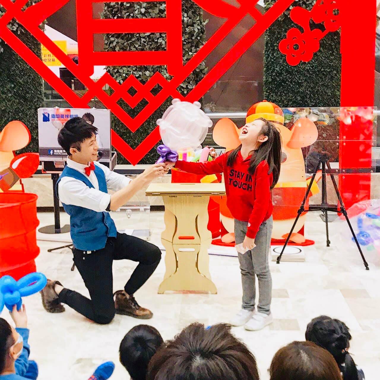 我單膝跪地，和穿紅色上衣的小女孩一起完成氣球魔術