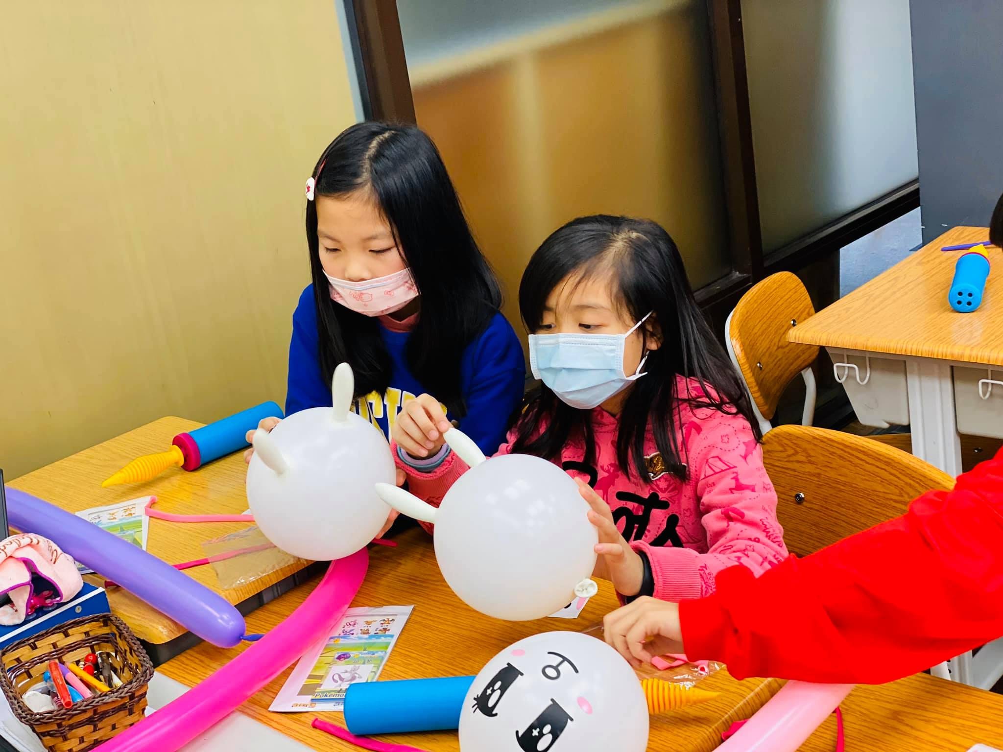 兩個戴口罩的女孩在桌上把白色圓氣球做成長耳朵造型