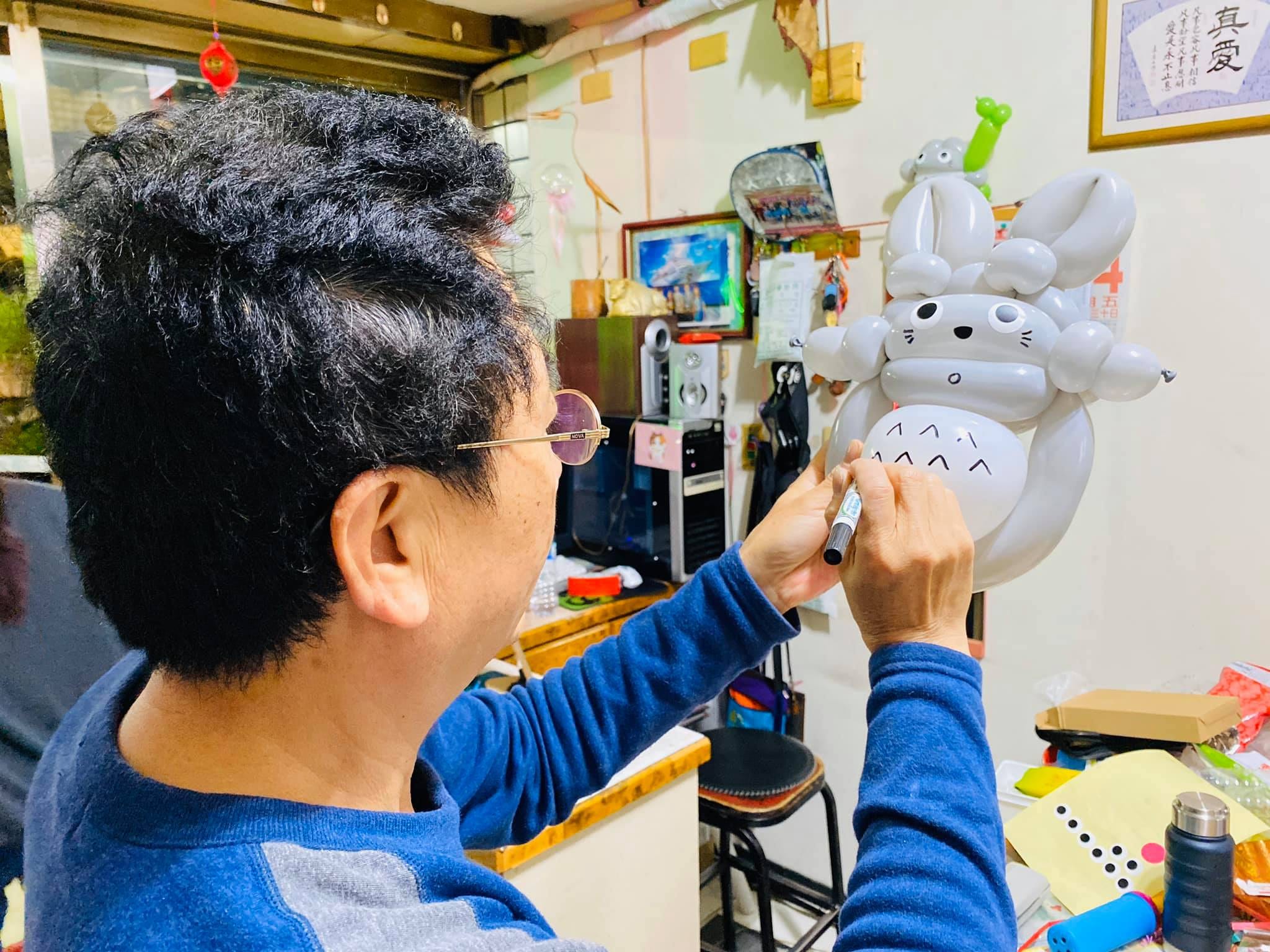 柯爹戴著眼鏡，用麥克筆在龍貓氣球的白肚子上畫花紋